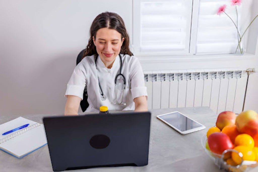 Healthcare provider smiling during a virtual consultation on a laptop with fresh fruit on the desk.