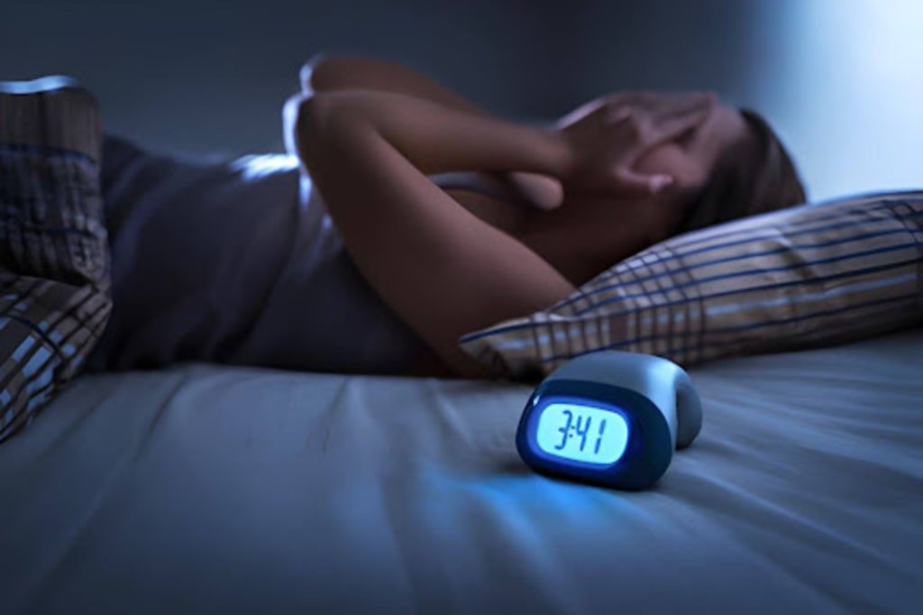Person lying awake in bed at night with an alarm clock showing 3:41, suggesting insomnia or sleep difficulty.