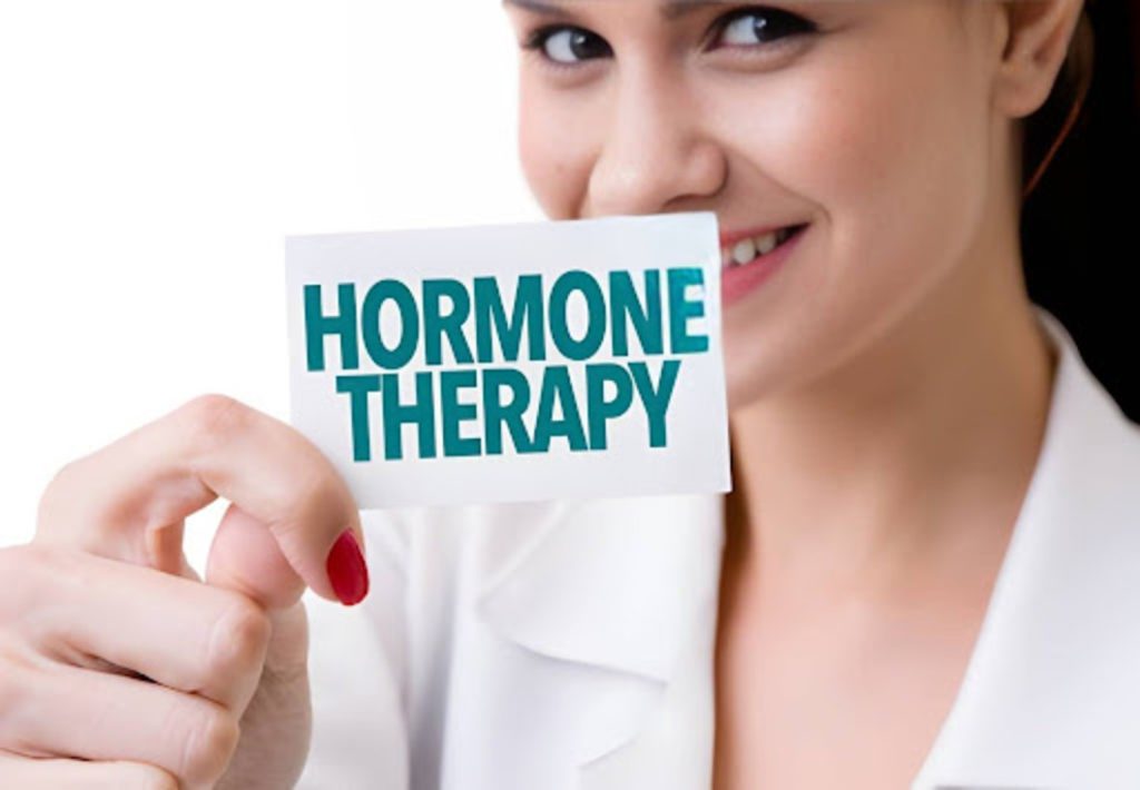Woman holding a card that says hormone therapy while smiling in a clinical wellness setting.