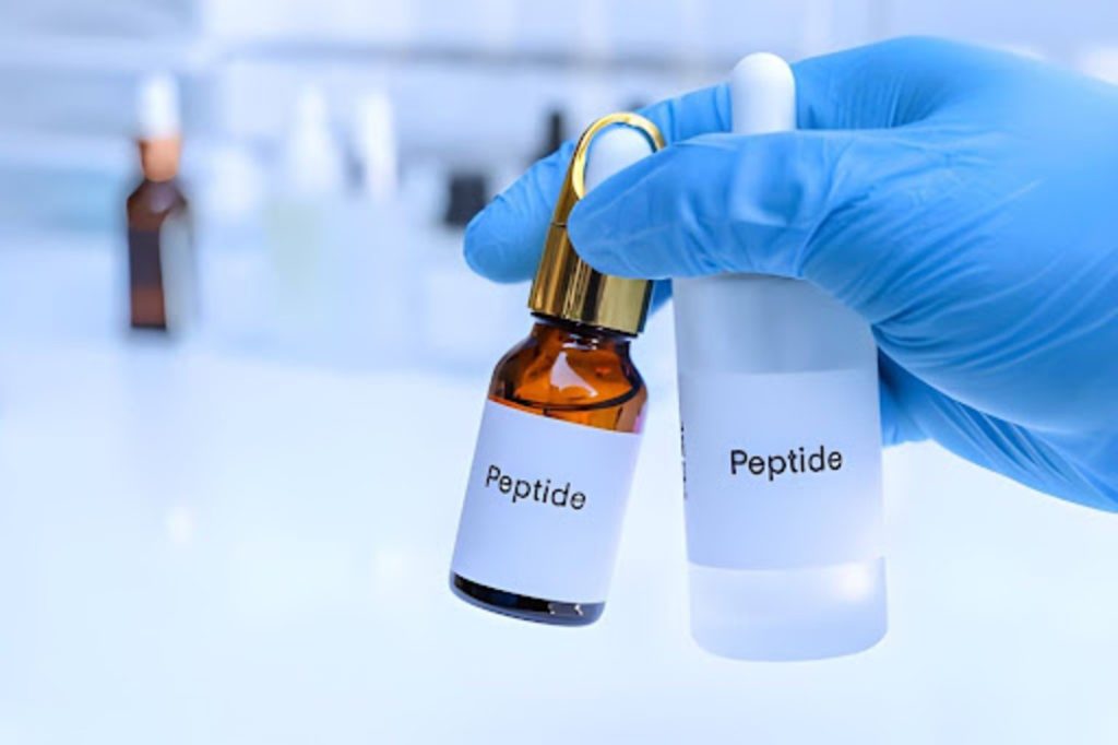 Gloved hand holding peptide bottles in a laboratory setting for peptide therapy and wellness treatment.
