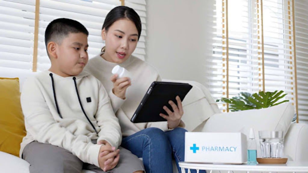 Mother reviewing pediatric medication instructions on a tablet while sitting with her child and a pharmacy kit at home.
