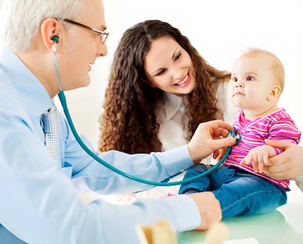 Pediatrician using a stethoscope to examine a smiling baby while the mother watches, holding the child during a routine checkup.