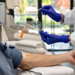 Healthcare professionals wearing gloves preparing an IV line for a patient seated in a clinic chair for hydration or nutrient therapy.